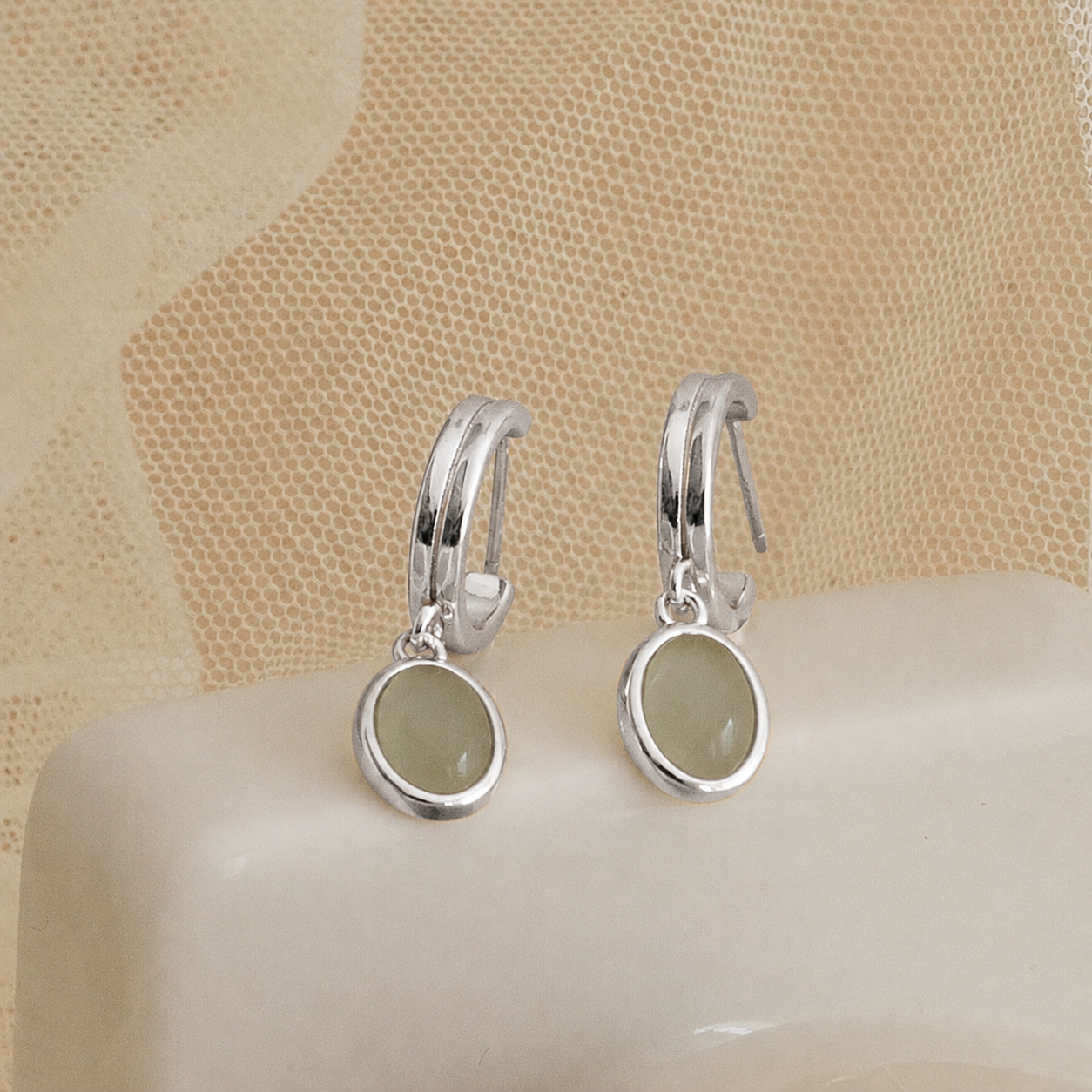Silver hoop earrings with green stones on a beige surface